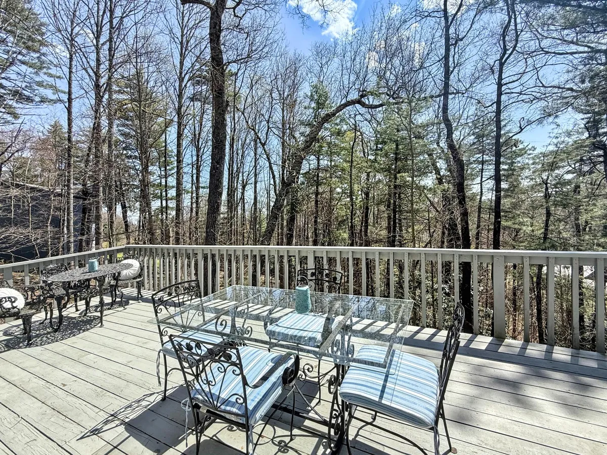 The scene features a glass-topped outdoor dining table surrounded by striped chairs, nestled among trees. The tranquil atmosphere emphasizes opportunities for outdoor meals and quiet moments spent enjoying the natural mountain environment.