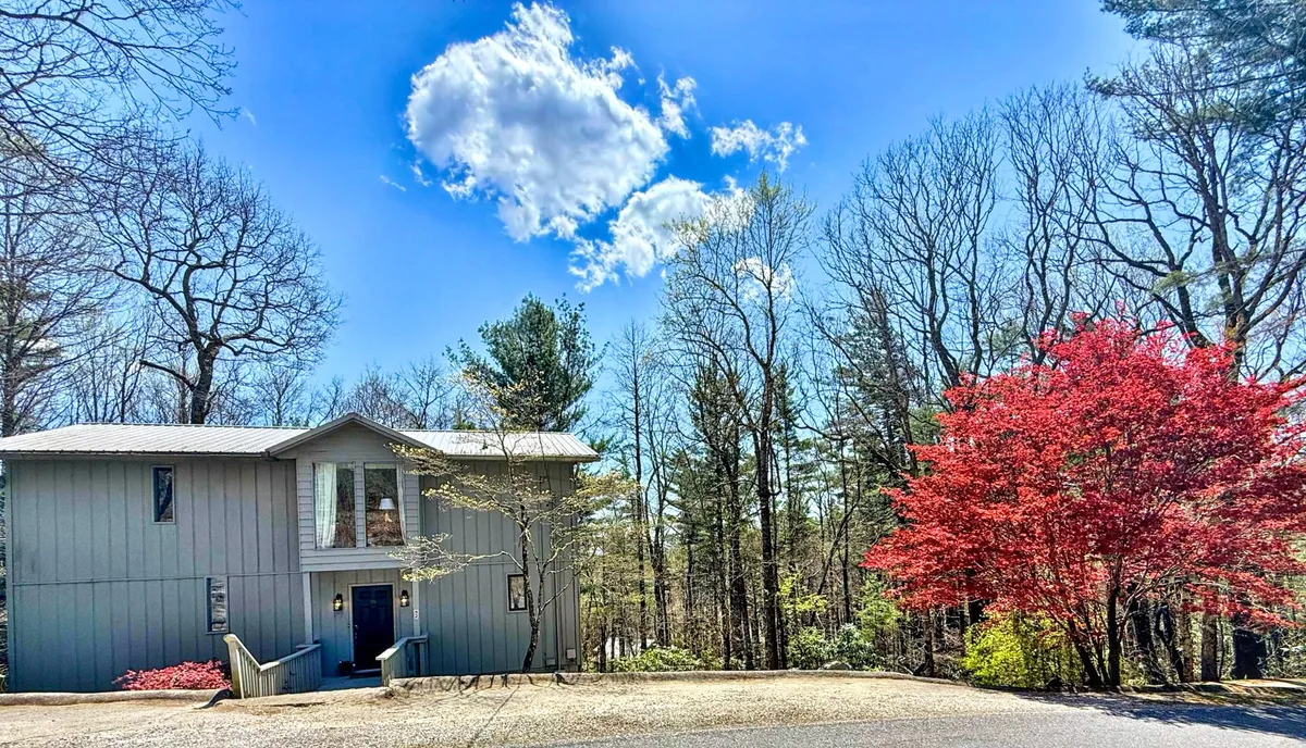 This image captures the exterior of the house set amidst vibrant red and green trees under a clear sky. The home is surrounded by nature and the expansive views suggest a tranquil yet accessible environment, illustrating the perfect blend of peaceful retreat and proximity to the lively town of Highlands.