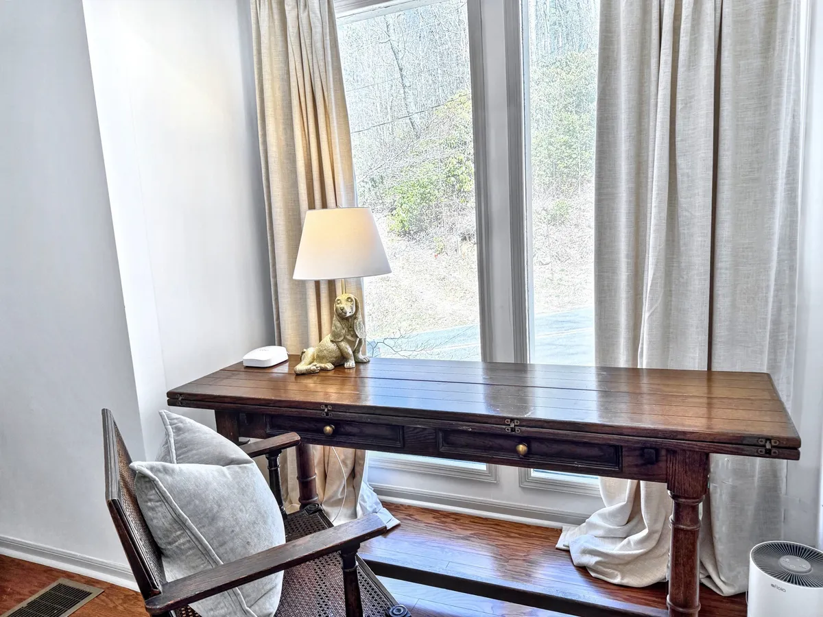 A calming, dedicated workspace with a wooden desk, comfortable chair, and warm lamp glow. Subtle decor and curtains frame the space, suggesting a peaceful spot ideal for focused remote work or creative pursuits, with hints of natural light streaming in.
